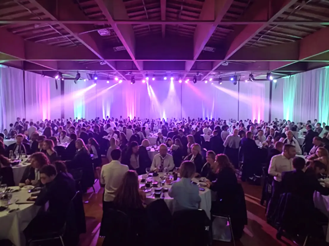 Cena aziendale elegante con ospiti seduti a tavoli rotondi durante un evento corporate con presentazione e intrattenimento.a Ascoli Piceno